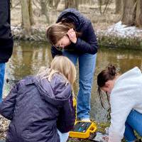 Careerline Tech Students crouching next to a backpack with data tech, outside in cold weather next to a creek